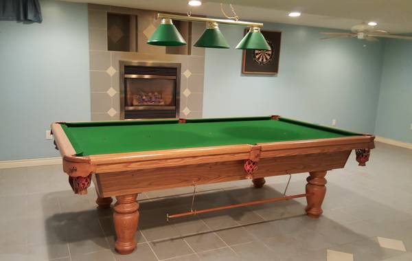Billiard room setting with green felt table, hanging lights, and fireplace