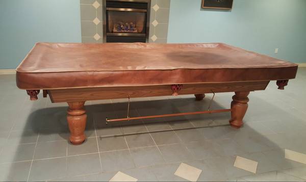 Covered pool table viewed from end with decorative fireplace in background