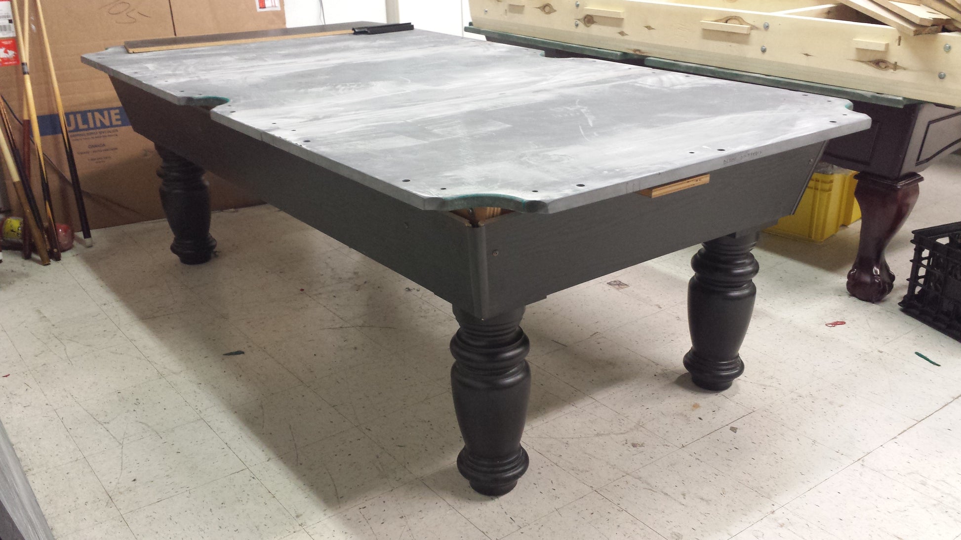 Pool table with gray dust cover and dark wood base in warehouse setting