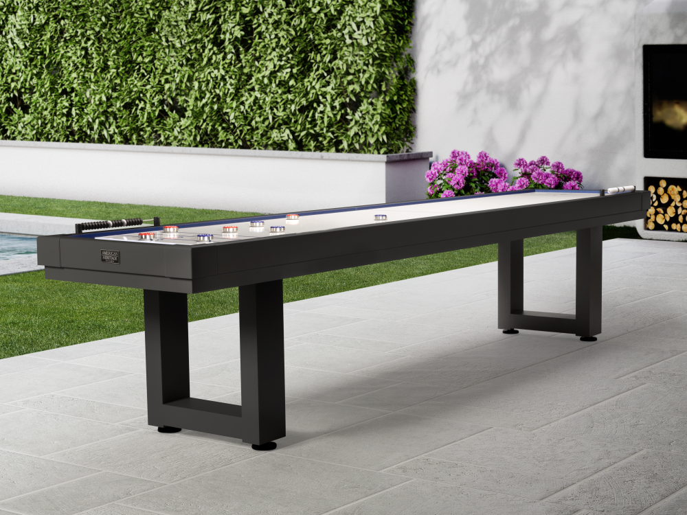 Black shuffleboard table on stone patio with purple flowering plants nearby